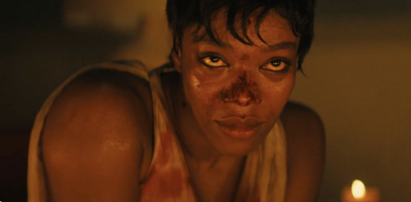 A bloodied woman in a candlelit room, kneeling with composure