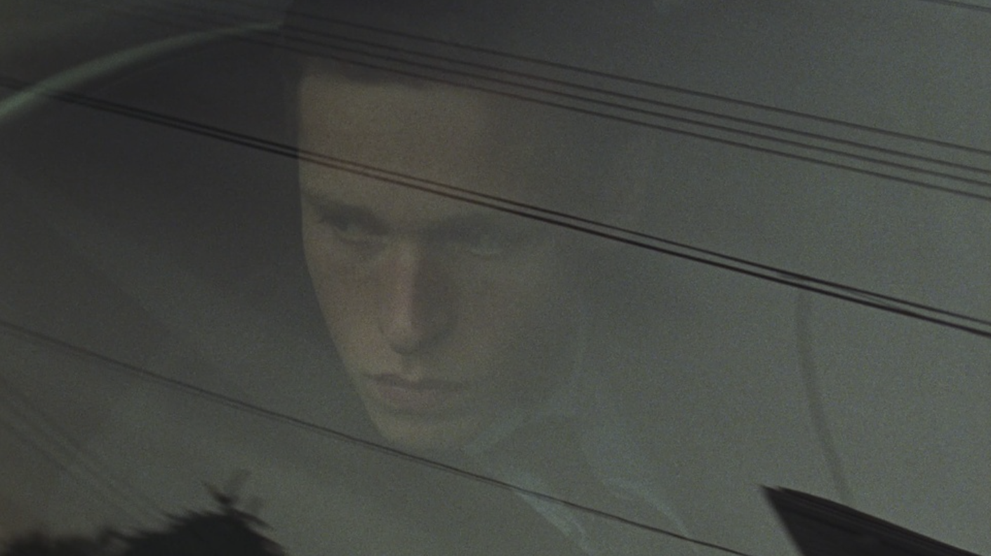 A young man’s reflection seen through a rain-streaked car window